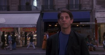 Movie still from “Bitter Moon” (1992), directed by Roman Polanski – A man standing on the sidewalk in front of a store; Medium shot, Over the shoulder angle