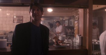 Movie still from “Bitter Moon” (1992), directed by Roman Polanski – A man standing in front of a counter in a kitchen; Medium shot, Over the shoulder angle