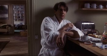 Movie still from “Bitter Moon” (1992), directed by Roman Polanski – A man sitting in a white bathrobe next to a table; Medium shot, Low angle