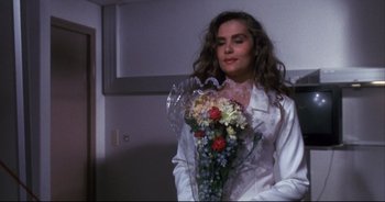 Movie still from “Bitter Moon” (1992), directed by Roman Polanski – A woman holding a bouquet of flowers while wearing a white robe; Medium shot, Over the shoulder angle