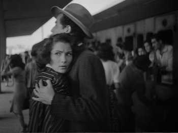 Movie still from “Bitter Rice” (1949), directed by Giuseppe De Santis – A man and a woman hugging in a crowd of onlookers; Medium shot, Over the shoulder angle