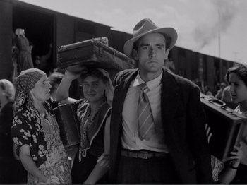 Movie still from “Bitter Rice” (1949), directed by Giuseppe De Santis – A man in a hat and a suit stands next to a woman in a hat; Medium shot, Low angle