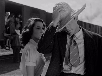 Movie still from “Bitter Rice” (1949), directed by Giuseppe De Santis – A man and a woman standing next to each other holding a hat; Medium shot, Low angle