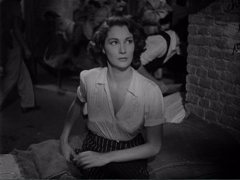 Movie still from “Bitter Rice” (1949), directed by Giuseppe De Santis – A woman sitting on the ground in front of a brick wall; Medium shot, Over the shoulder angle