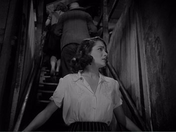 Movie still from “Bitter Rice” (1949), directed by Giuseppe De Santis – A woman standing on some stairs in a building; Medium shot, Low angle