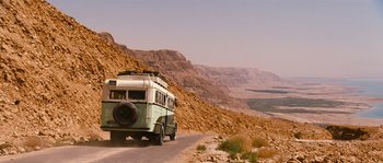 Movie still from “Black Book” (2006), directed by Paul Verhoeven – A bus is driving down a road in the desert; Extreme Wide shot, Low angle