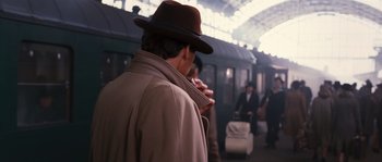 Movie still from “Black Book” (2006), directed by Paul Verhoeven – A man in a hat smoking a cigarette at a train station; Medium shot, Over the shoulder angle