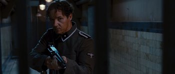 Movie still from “Black Book” (2006), directed by Paul Verhoeven – A man in a uniform holding a gun in a dark room; Medium shot, Low angle