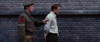 Movie still from “Black Book” (2006), directed by Paul Verhoeven – A man in a white shirt is being handcuffed by another man; Medium shot, Low angle
