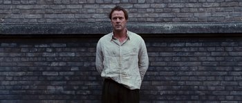 Movie still from “Black Book” (2006), directed by Paul Verhoeven – A man standing in front of a brick wall with his hands in his pockets; Medium shot, Low angle