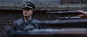 Movie still from “Black Book” (2006), directed by Paul Verhoeven – A man in a military uniform is sitting outside; Medium shot, Over the shoulder angle