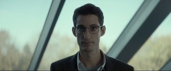 Movie still from “Black Box” (2021), directed by Yann Gozlan – A person wearing glasses and a suit; Close Up shot, Low angle