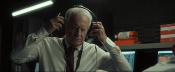 Movie still from “Black Box” (2021), directed by Yann Gozlan – An older man wearing headphones while holding his head; Close Up shot, High angle