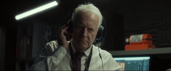Movie still from “Black Box” (2021), directed by Yann Gozlan – An older man wearing headphones while talking on the phone; Close Up shot, Over the shoulder angle