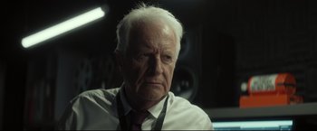 Movie still from “Black Box” (2021), directed by Yann Gozlan – An older man with white hair wearing a white shirt and a red tie; Close Up shot, Over the shoulder angle