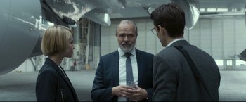Movie still from “Black Box” (2021), directed by Yann Gozlan – A man in a suit talks to two other men; Medium shot, Over the shoulder angle