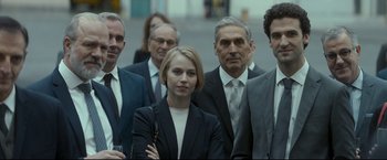Movie still from “Black Box” (2021), directed by Yann Gozlan – A group of people in business attire standing together; Medium shot, Over the shoulder angle
