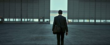 Movie still from “Black Box” (2021), directed by Yann Gozlan – A man in a black suit and a brown bag; Wide shot, Over the shoulder angle