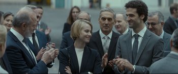 Movie still from “Black Box” (2021), directed by Yann Gozlan – A group of people in business attire clapping; Medium shot, Over the shoulder angle