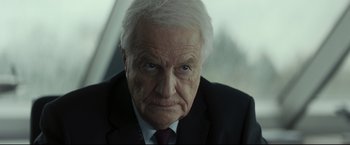Movie still from “Black Box” (2021), directed by Yann Gozlan – An older man wearing a suit and tie; Close Up shot, Over the shoulder angle