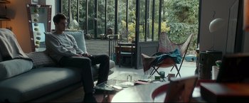 Movie still from “Black Box” (2021), directed by Yann Gozlan – A man sitting on a chair in a living room next to a window; Wide shot, Over the shoulder angle