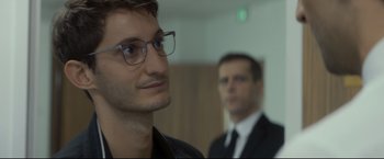 Movie still from “Black Box” (2021), directed by Yann Gozlan – A man in a suit and glasses looking at the camera; Close Up shot, Over the shoulder angle