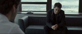 Movie still from “Black Box” (2021), directed by Yann Gozlan – A man sitting on top of a couch in a living room; Medium shot, Over the shoulder angle