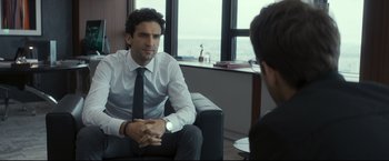 Movie still from “Black Box” (2021), directed by Yann Gozlan – A man sitting in front of another man in an office setting; Medium shot, Over the shoulder angle