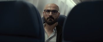 Movie still from “Black Box” (2021), directed by Yann Gozlan – A man with a beard and glasses on a plane; Close Up shot, Over the shoulder angle