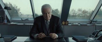 Movie still from “Black Box” (2021), directed by Yann Gozlan – An older man sitting at a table in front of a window; Medium shot, Over the shoulder angle