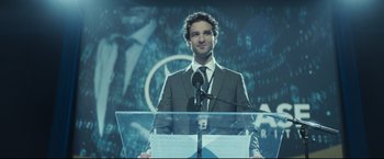 Movie still from “Black Box” (2021), directed by Yann Gozlan – A man standing at a podium speaking to a crowd; Medium shot, Low angle