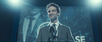 Movie still from “Black Box” (2021), directed by Yann Gozlan – A man standing at a microphone in front of an audience; Close Up shot, Over the shoulder angle