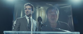 Movie still from “Black Box” (2021), directed by Yann Gozlan – A man standing next to a microphone in front of another man; Medium shot, Low angle