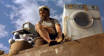 Movie still from “Black Cat, White Cat” (1998), directed by Emir Kusturica – A man sitting on top of a pile of garbage; Wide shot, Low angle