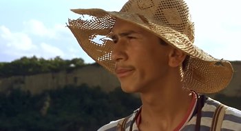 Movie still from “Black Cat, White Cat” (1998), directed by Emir Kusturica – A person wearing a straw hat; Close Up shot, Low angle