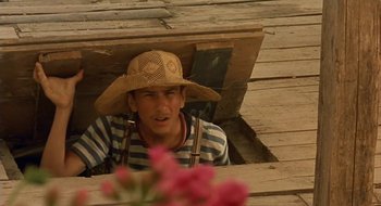 Movie still from “Black Cat, White Cat” (1998), directed by Emir Kusturica – A man wearing a straw hat sitting on a porch; Medium shot, High angle