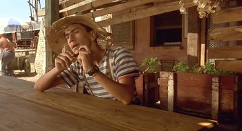Movie still from “Black Cat, White Cat” (1998), directed by Emir Kusturica – A man wearing a straw cowboy hat is sitting at a table; Medium shot, Low angle