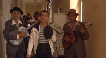 Movie still from “Black Cat, White Cat” (1998), directed by Emir Kusturica – A group of men in a hallway playing music instruments; Medium shot, Low angle