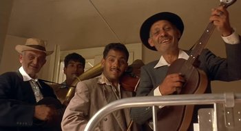 Movie still from “Black Cat, White Cat” (1998), directed by Emir Kusturica – A group of men standing next to each other on a street; Medium shot, Low angle