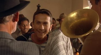 Movie still from “Black Cat, White Cat” (1998), directed by Emir Kusturica – A young man smiles as he plays a brass instrument; Close Up shot, Low angle