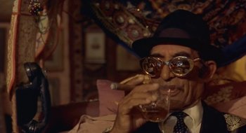 Movie still from “Black Cat, White Cat” (1998), directed by Emir Kusturica – An older man wearing a hat and smoking a cigarette; Close Up shot, High angle