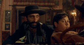 Movie still from “Black Cat, White Cat” (1998), directed by Emir Kusturica – A man with a beard and a hat is smoking a pipe; Close Up shot, Over the shoulder angle