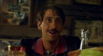 Movie still from “Black Cat, White Cat” (1998), directed by Emir Kusturica – A person sitting at a table with food; Close Up shot, Low angle