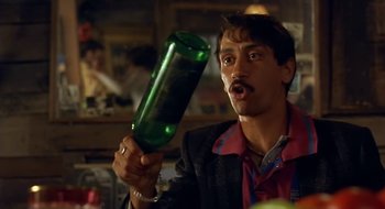 Movie still from “Black Cat, White Cat” (1998), directed by Emir Kusturica – A man is holding a large bottle of wine; Close Up shot, Low angle