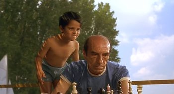 Movie still from “Black Cat, White Cat” (1998), directed by Emir Kusturica – An older man and a young boy playing a game of chess; Medium shot, Low angle