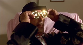 Movie still from “Black Cat, White Cat” (1998), directed by Emir Kusturica – A man wearing a hat and glasses with a light on his head; Close Up shot, Low angle