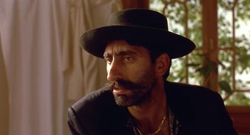 Movie still from “Black Cat, White Cat” (1998), directed by Emir Kusturica – A man wearing a black hat and a black shirt; Close Up shot, Low angle