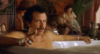 Movie still from “Black Cat, White Cat” (1998), directed by Emir Kusturica – A man sitting in a bathtub with a ring around his neck; Medium shot, Low angle