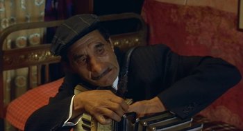 Movie still from “Black Cat, White Cat” (1998), directed by Emir Kusturica – An older man wearing a hat is leaning on an accordion; Close Up shot, High angle