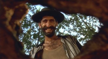 Movie still from “Black Cat, White Cat” (1998), directed by Emir Kusturica – A man with a beard wearing a hat and smiling; Close Up shot, Low angle